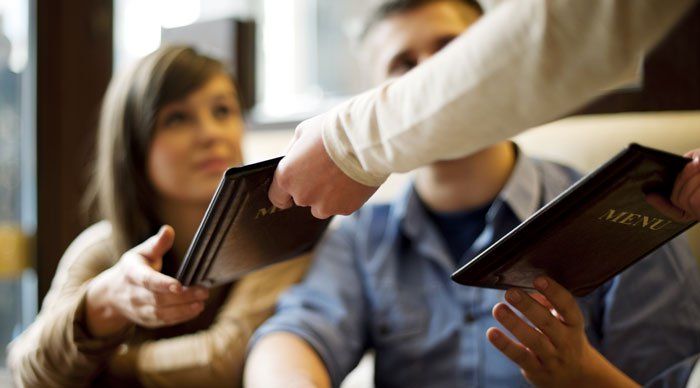 a couple customers is handed restaurant menu by a waiter